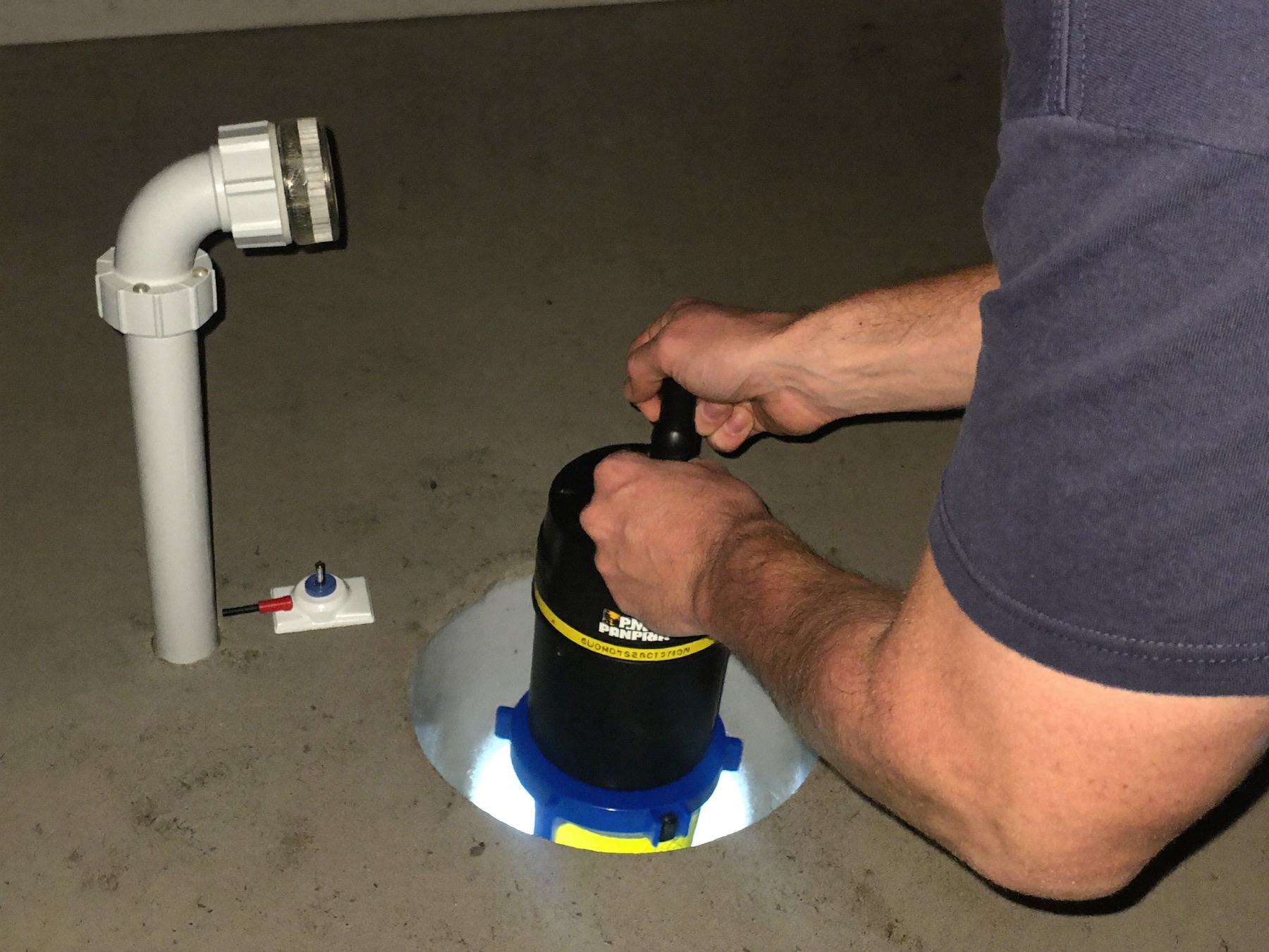 A Hartwell plumber seating a new sump pump in a basement pit, check valve and discharge line in frame